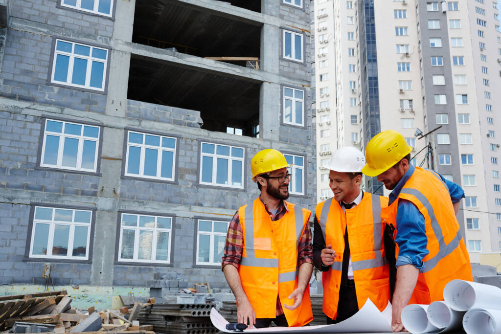 Construction engineers reviewing blueprints at a building site with safety helmets